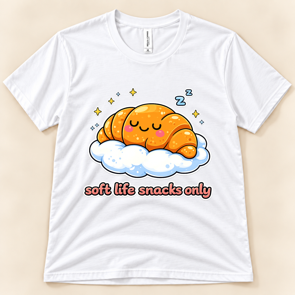 White Bella Canvas 3001 kawaii pastry graphic tee featuring a cute smiling croissant sleeping on a blue and white cloud with stars and Soft Life Snacks Only saying from New Chapter Tees, a California small business.