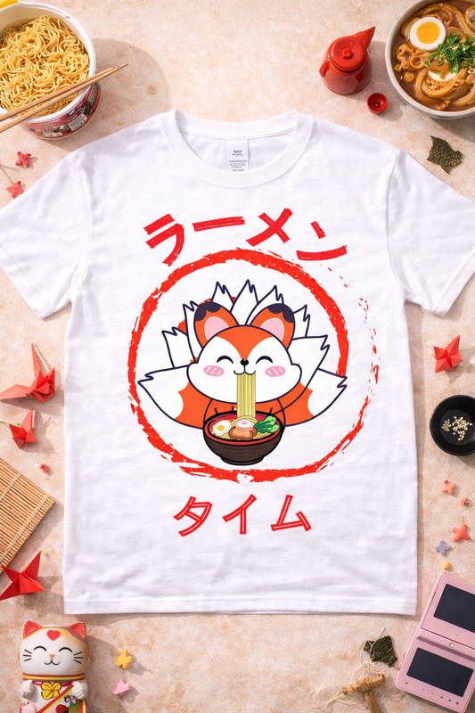 White graphic t-shirt featuring kawaii fox eating ramen with Japanese text, styled in a cozy flatlay with ramen bowls and cute themed accessories