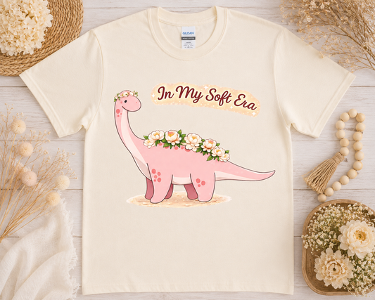 Cute floral dinosaur graphic tee on natural Gildan shirt with soft cottagecore flower flatlay styling
