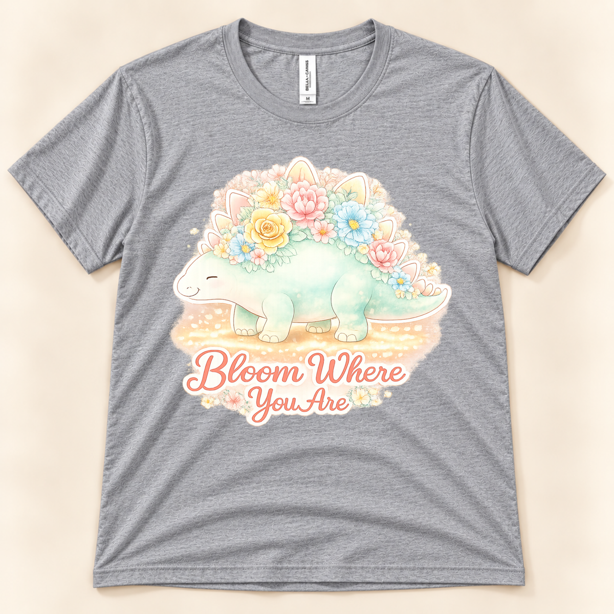 Bloom Where You Are Stegosaurus graphic tee in Athletic Heather featuring a cute pastel dinosaur covered in colorful flowers from New Chapter Tees, a California small business.