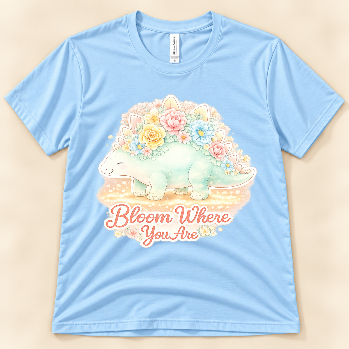 Bloom Where You Are Stegosaurus graphic tee in Baby Blue featuring a kawaii pastel floral dinosaur and inspirational quote from New Chapter Tees, a California small business.