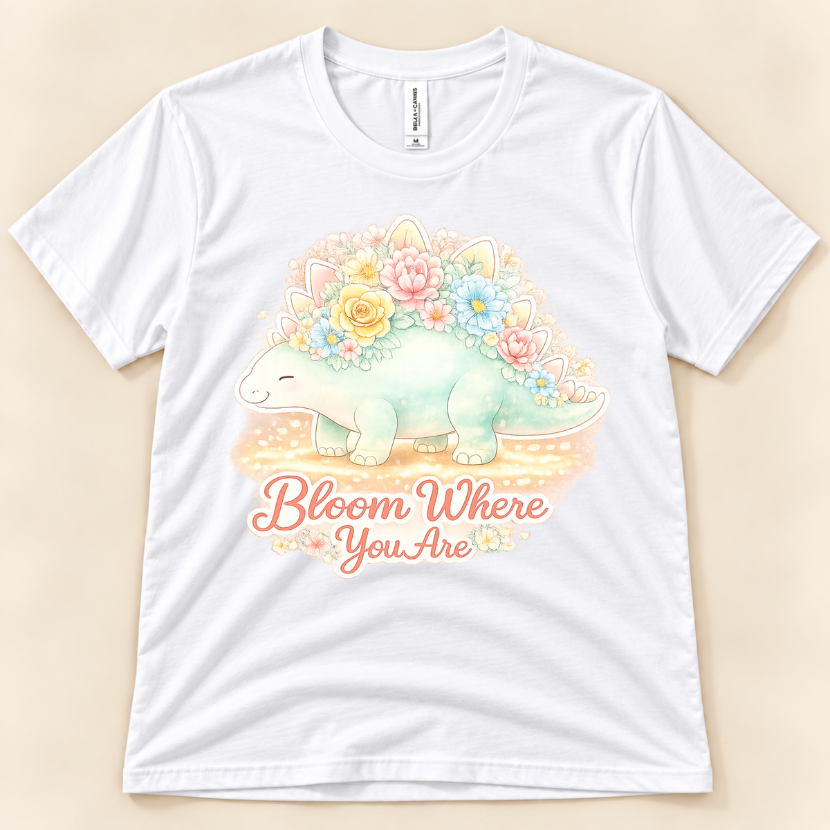 Bloom Where You Are Stegosaurus graphic tee in White featuring a pastel stegosaurus covered in colorful flowers with an uplifting quote from New Chapter Tees, a California small business.