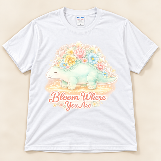 Bloom Where You Are Stegosaurus graphic tee in White featuring a pastel floral dinosaur and uplifting Bloom Where You Are quote from New Chapter Tees, a California small business.
