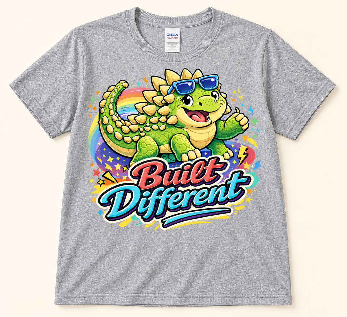 Sport Gray Gildan 5000 Built Different Ankylosaurus Tee featuring a cute green dinosaur, rainbow and bold lettering