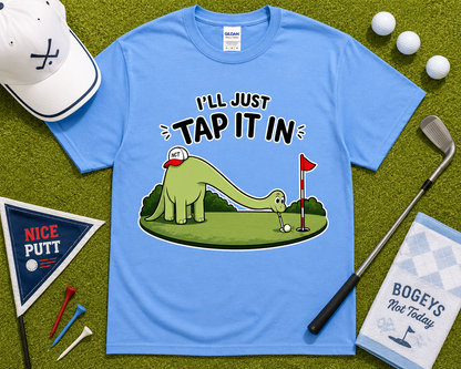 Carolina Blue golf dinosaur shirt flatlay with funny Ill Just Tap It In brontosaurus golfer design on golf course inspired grass background unique golf gift USA