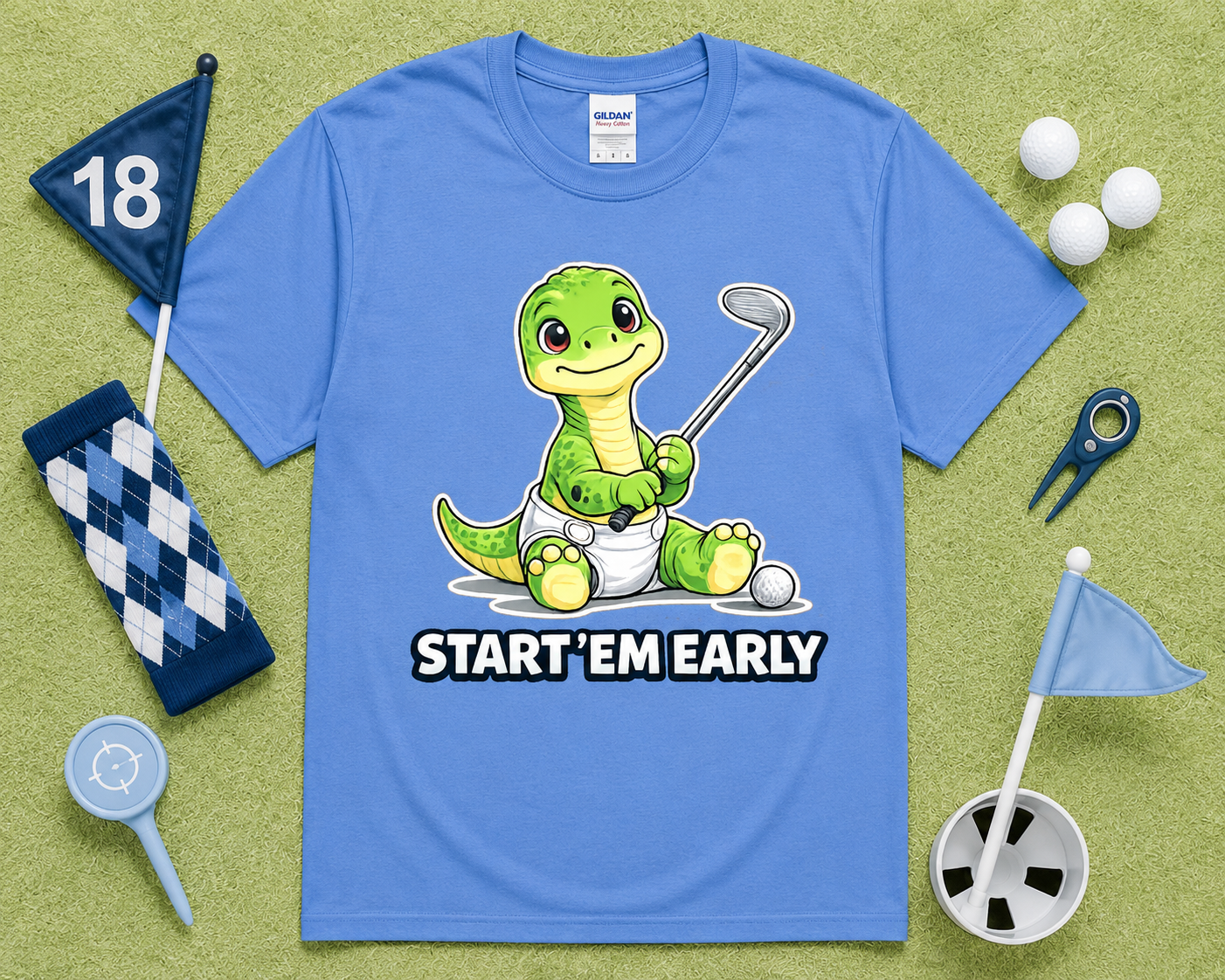 Carolina Blue Gildan 5000 dinosaur golf shirt flatlay with golf accessories on light green grass, funny Start Em Early golf tee for kids, golfers, parents and golf lovers in the USA.
