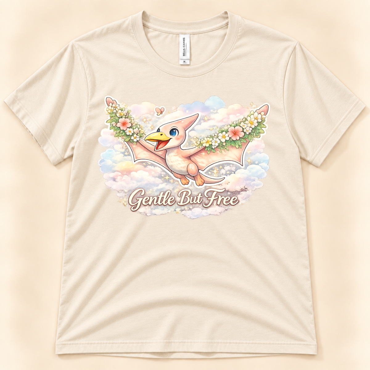 Gentle But Free pterodactyl graphic tee in Natural featuring a cute floral dinosaur flying through pastel clouds from New Chapter Tees, a California small business.