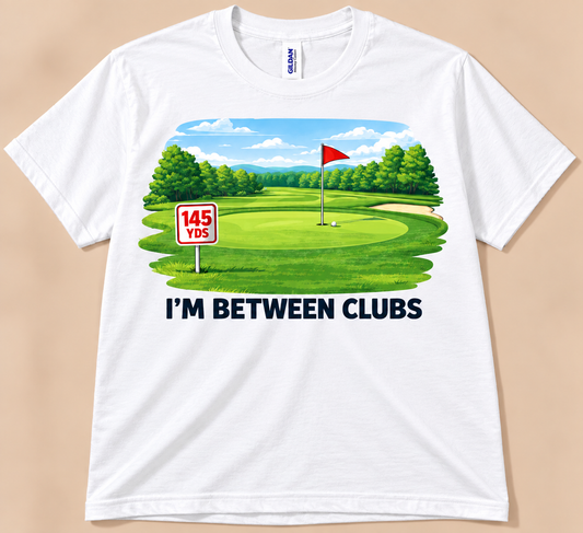 White Gildan 5000 I’m Between Clubs Tee featuring golf course, red flag, 145 yard sign and funny golf quote