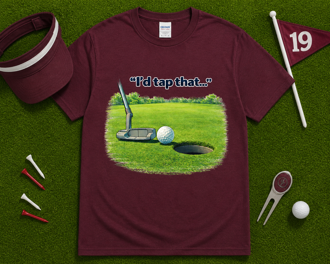 Maroon golf graphic tee flatlay featuring I'd Tap That golf putting artwork with golf accessories, humorous golf gift shirt for golfers throughout the USA.