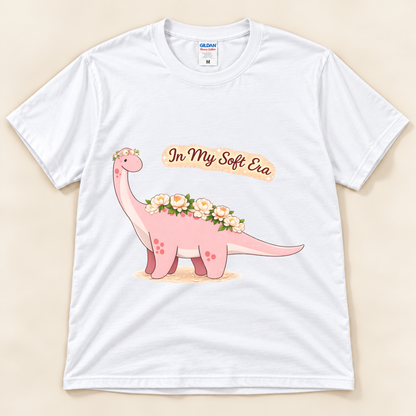 White Gildan 5000 In My Soft Era dinosaur graphic tee featuring a cute pink Brontosaurus with floral details and soft life artwork from New Chapter Tees, a California small business.