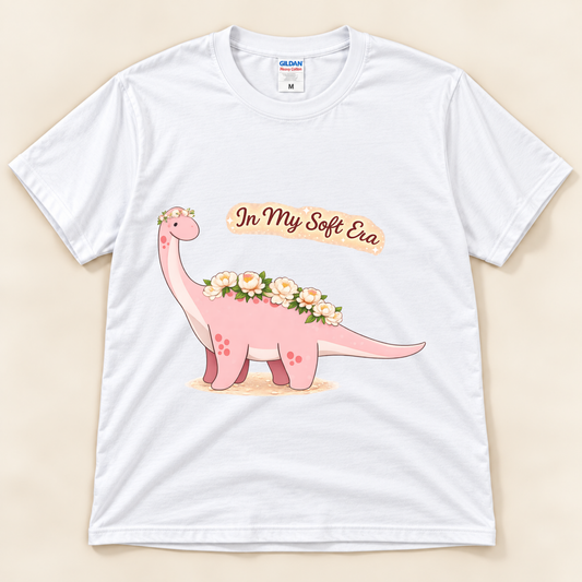 White Gildan 5000 In My Soft Era dinosaur graphic tee featuring a cute pink Brontosaurus with floral details and soft life artwork from New Chapter Tees, a California small business.