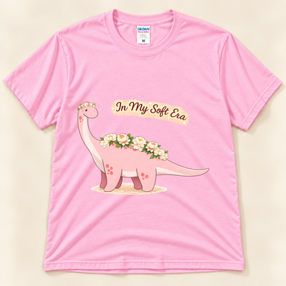 Light Pink Gildan 5000 In My Soft Era dinosaur tee featuring a cute pink Brontosaurus with floral details and a cozy soft life theme from New Chapter Tees, a California small business.