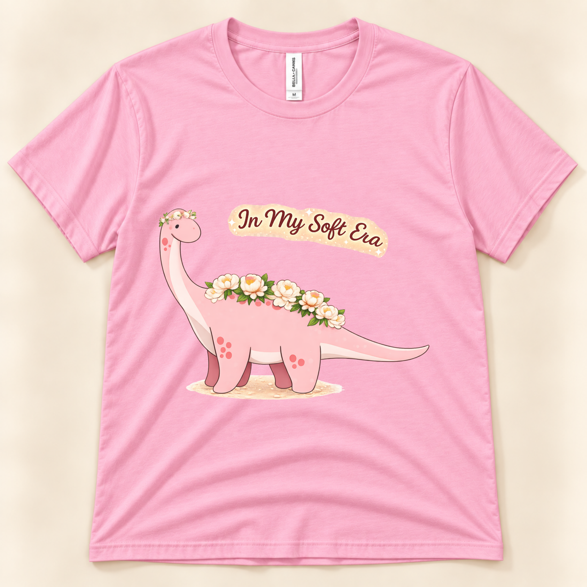 Pink Bella Canvas 3001 In My Soft Era graphic tee featuring a cute pink Brontosaurus decorated with delicate flowers from New Chapter Tees, a California small business.