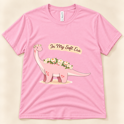 Pink Bella Canvas 3001 In My Soft Era graphic tee featuring a cute pink Brontosaurus decorated with delicate flowers from New Chapter Tees, a California small business.
