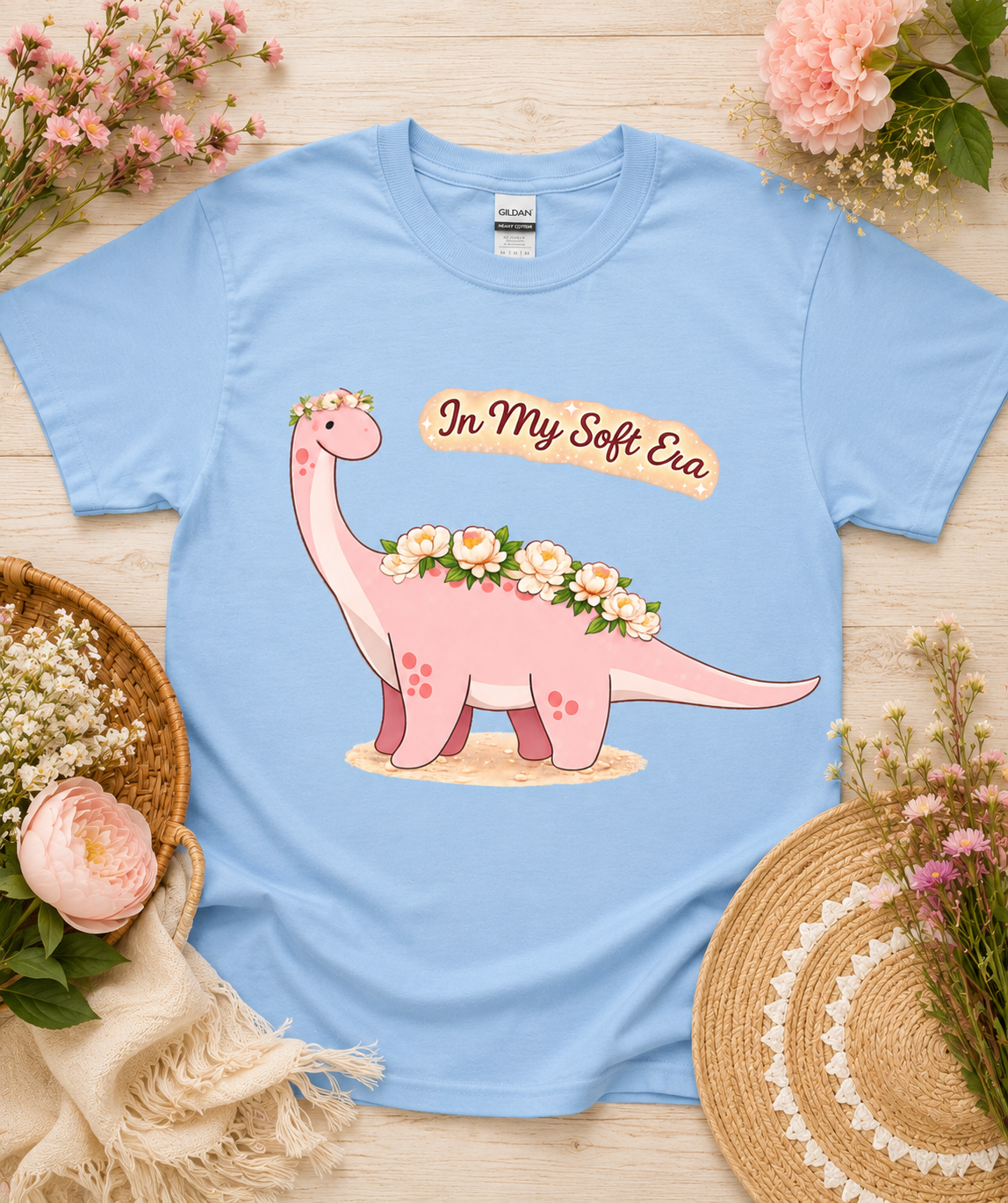 Cute pink dinosaur graphic tee on Carolina Blue Gildan 5000 shirt with In My Soft Era floral dinosaur artwork whimsical aesthetic gift for dinosaur lovers