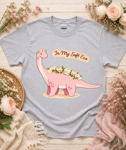 Cute floral dinosaur graphic tee on Sport Gray Gildan 5000 shirt featuring In My Soft Era pink dinosaur artwork cozy aesthetic gift for women USA