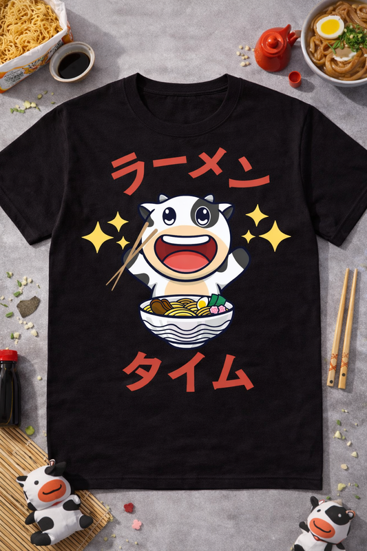 Black graphic tee featuring a kawaii cow eating ramen with Japanese text, styled with ramen bowls, chopsticks, soy sauce, and cute cow-themed flatlay props.