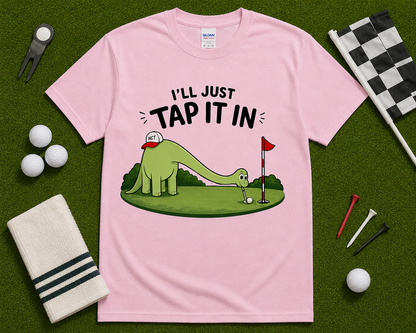 Light Pink golf dinosaur shirt flatlay with Ill Just Tap It In funny brontosaurus golfer graphic on golf themed grass background cute golf gift USA