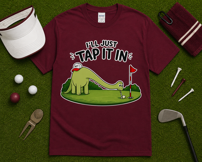 Maroon golf dinosaur shirt flatlay with Ill Just Tap It In putting dinosaur graphic on golf course inspired grass background funny golfer gift idea USA