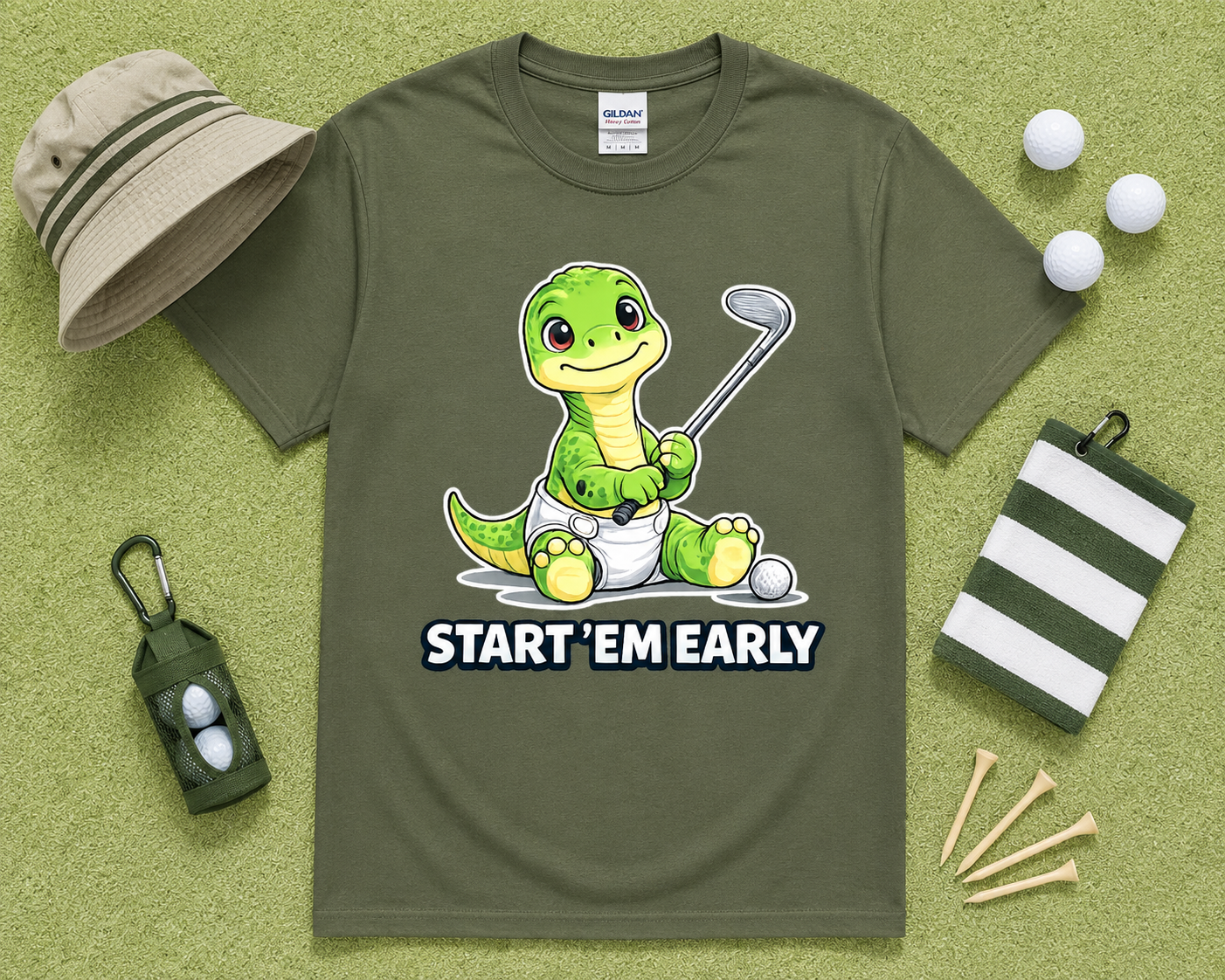 Military Green Gildan 5000 funny dinosaur golf shirt flatlay with golf accessories on light green grass, Start Em Early golf graphic tee for golfers, dads and golf families throughout the USA.