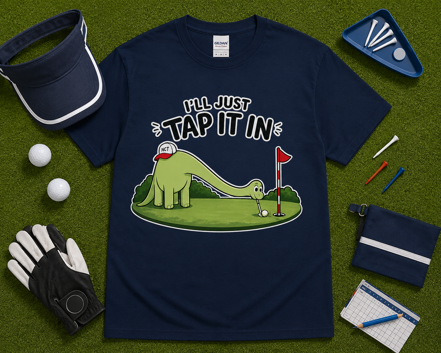 Navy blue golf dinosaur shirt flatlay featuring Ill Just Tap It In brontosaurus golf graphic on golf themed grass background funny golf apparel gift USA