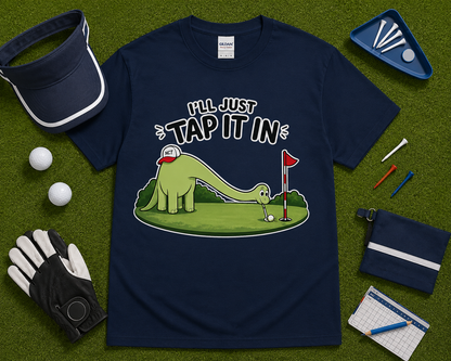 Navy blue golf dinosaur shirt flatlay featuring Ill Just Tap It In brontosaurus golf graphic on golf themed grass background funny golf apparel gift USA