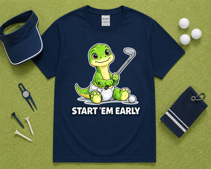 Navy Gildan 5000 funny dinosaur golf shirt flatlay with golf accessories on light green grass, cute Start Em Early golf tee gift for golfers, dads, kids and golf families in the USA.