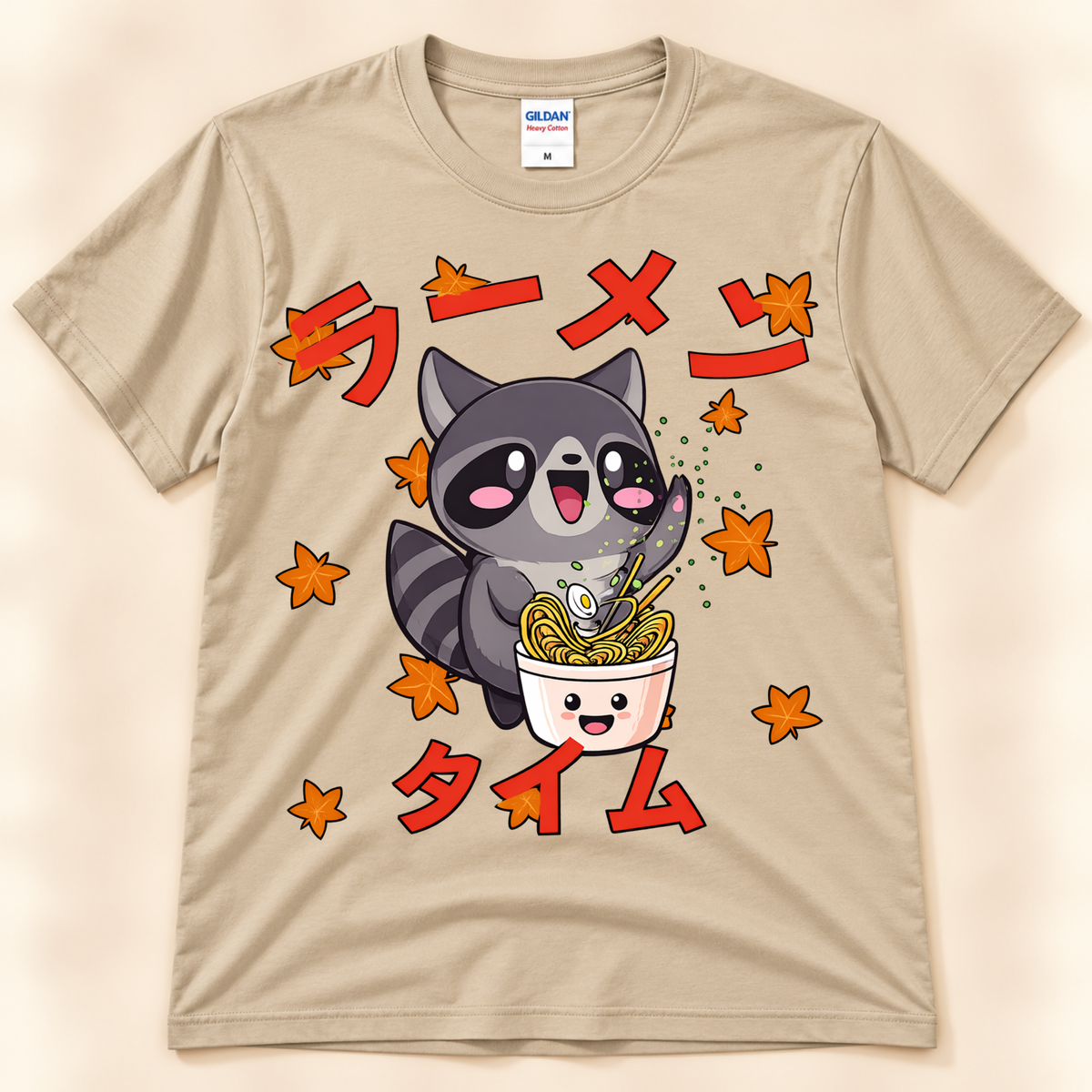 Sand Gildan 5000 raccoon ramen graphic tee featuring a kawaii raccoon eating noodles with autumn leaves and Japanese Ramen Time artwork.