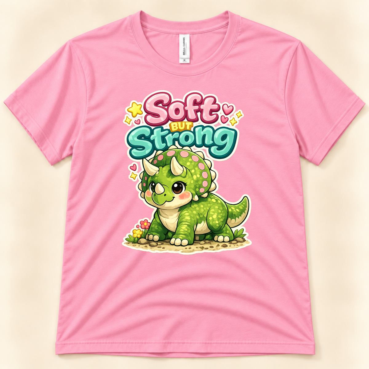 Soft But Strong cute triceratops graphic tee in Charity Pink by New Chapter Tees, a California small business, featuring a colorful kawaii dinosaur design.