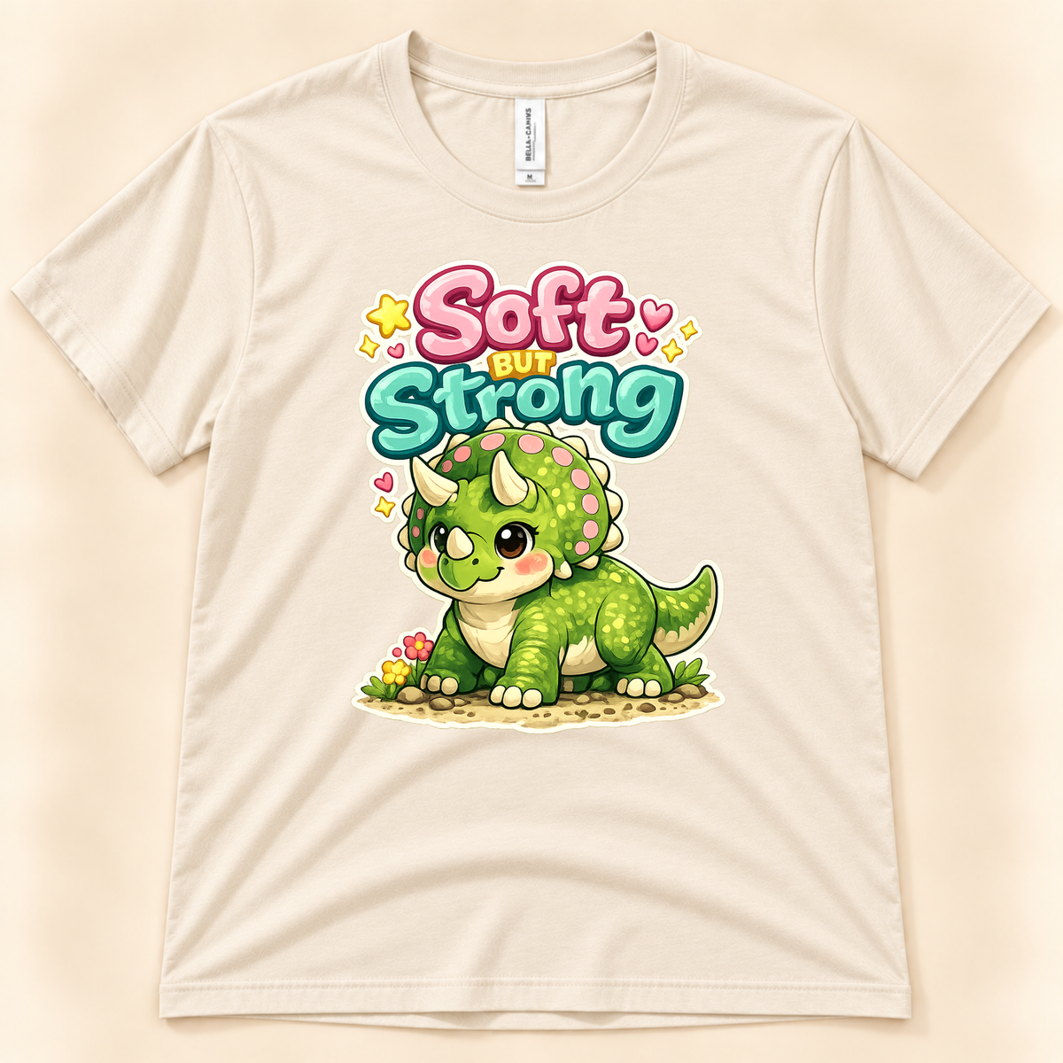 Soft But Strong triceratops graphic tee in Natural by New Chapter Tees, a California small business, with a cute green dinosaur and colorful lettering.