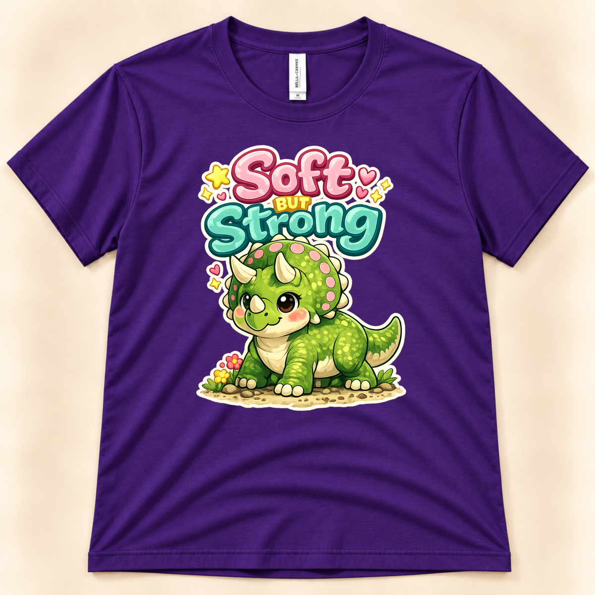 Soft But Strong cute dinosaur graphic tee in Team Purple by New Chapter Tees, a California small business, featuring a green kawaii triceratops.