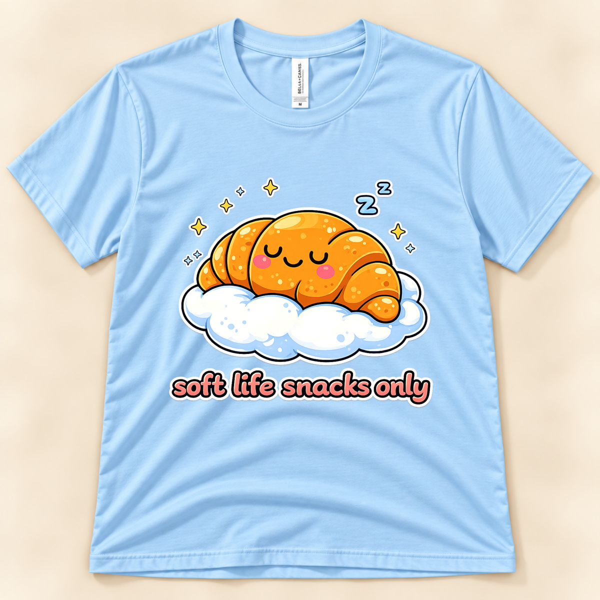 Baby Blue Bella Canvas 3001 graphic tee featuring a cute sleeping croissant on a fluffy cloud with stars and Soft Life Snacks Only lettering from New Chapter Tees, a California small business.