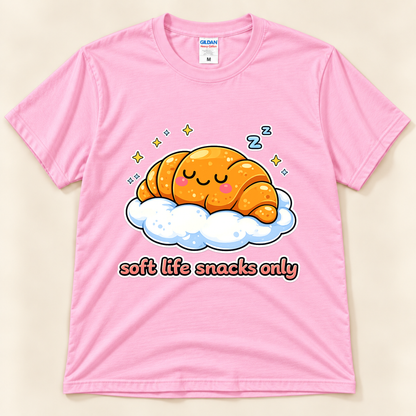 Light Pink Gildan 5000 kawaii food graphic tee featuring a sleepy golden croissant resting on a fluffy cloud with stars and Soft Life Snacks Only lettering from New Chapter Tees, a California small business.