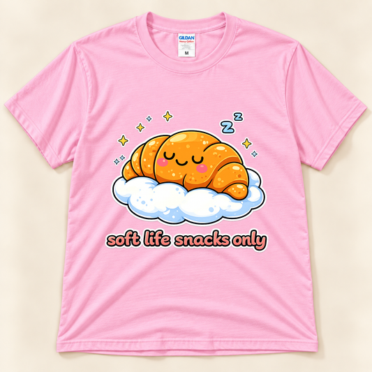 Light Pink Gildan 5000 kawaii food graphic tee featuring a sleepy golden croissant resting on a fluffy cloud with stars and Soft Life Snacks Only lettering from New Chapter Tees, a California small business.