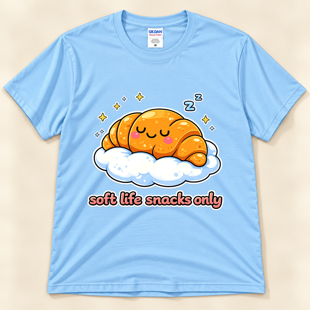 Light Blue Gildan 5000 cute croissant graphic tee featuring a smiling sleepy pastry on a cloud with yellow sparkles, blue Z symbols, and Soft Life Snacks Only saying from New Chapter Tees, a California small business.