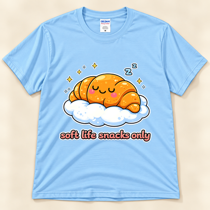 Light Blue Gildan 5000 cute croissant graphic tee featuring a smiling sleepy pastry on a cloud with yellow sparkles, blue Z symbols, and Soft Life Snacks Only saying from New Chapter Tees, a California small business.
