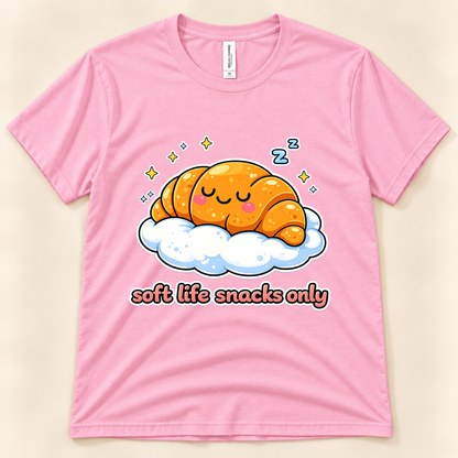Pink Bella Canvas 3001 cute foodie graphic tee featuring a sleepy orange croissant resting on a fluffy cloud with sparkles and Soft Life Snacks Only lettering from New Chapter Tees, a California small business.