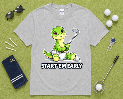 Sport Gray Gildan 5000 cute dinosaur golf shirt flatlay with golf accessories on light green grass, funny Start Em Early golf graphic tee for golfers, dads, moms and families in the USA.