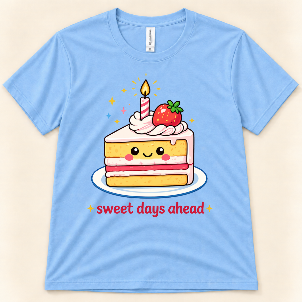 Carolina Blue Bella Canvas 3001 kawaii cake graphic tee featuring a smiling strawberry cake slice, birthday candle, colorful sparkles, and Sweet Days Ahead lettering from New Chapter Tees, a California small business.