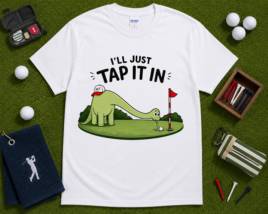 White golf dinosaur shirt flatlay featuring Ill Just Tap It In brontosaurus putting graphic on golf themed grass background funny golfer gift shirt for men women and kids USA