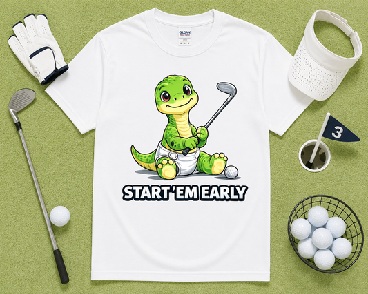 White Gildan 5000 Start Em Early dinosaur golf shirt flatlay with golf accessories on light green grass, funny golf graphic tee gift for junior golfers, parents and golf lovers across the USA.