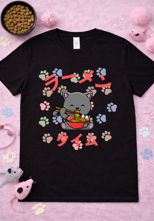 Kawaii gray cat ramen graphic tee on black shirt featuring cute cartoon cat eating noodles with chopsticks, colorful paw prints, Japanese ramen text, anime foodie design flatlay with cat toys and yarn