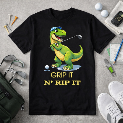 Funny dinosaur golf shirt with Grip It N Rip It text and T Rex golfer graphic on black and white tee flatlay with golf accessories
