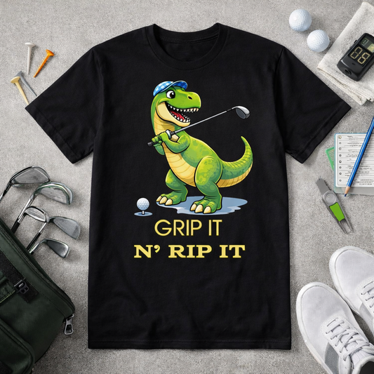Funny dinosaur golf shirt with Grip It N Rip It text and T Rex golfer graphic on black and white tee flatlay with golf accessories