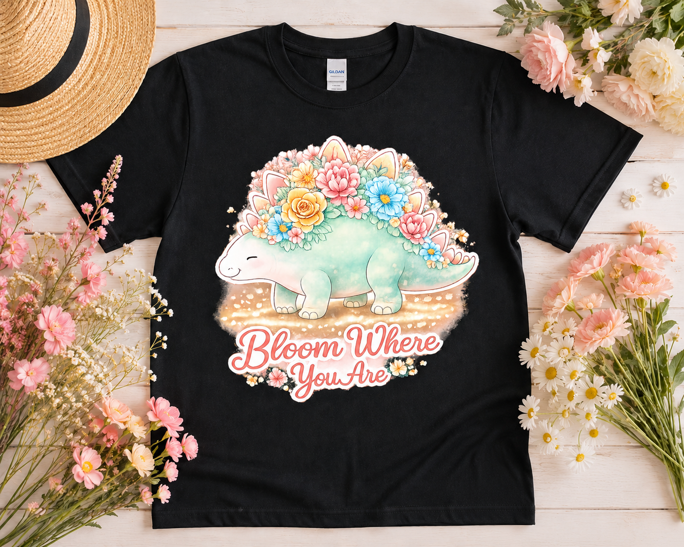Bloom Where You Are floral stegosaurus graphic tee on black Gildan shirt flatlay with pink flowers and cottagecore aesthetic props