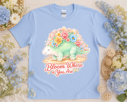 Bloom Where You Are pastel dinosaur graphic tee on Carolina blue Gildan shirt with blue floral flatlay styling