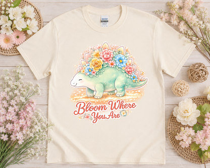 Bloom Where You Are watercolor floral dinosaur graphic tee on natural Gildan shirt with neutral floral flatlay styling