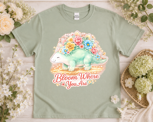 Bloom Where You Are pastel stegosaurus graphic tee on sage green Gildan shirt with soft floral aesthetic props
