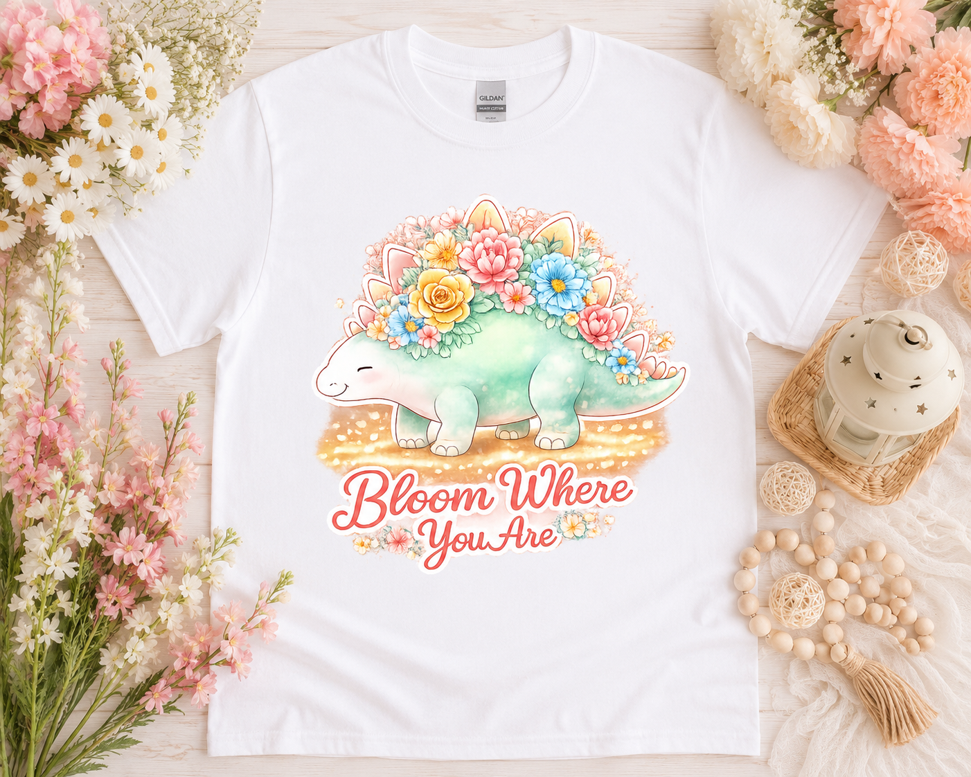 Bloom Where You Are cute floral dinosaur graphic tee on white Gildan shirt with pastel flower flatlay aesthetic