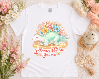 Bloom Where You Are cute floral dinosaur graphic tee on white Gildan shirt with pastel flower flatlay aesthetic